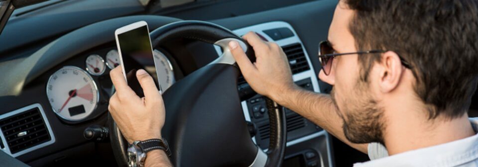 A young, Caucasian man using his cellphone while driving to illustrate how distracted driving looks like.