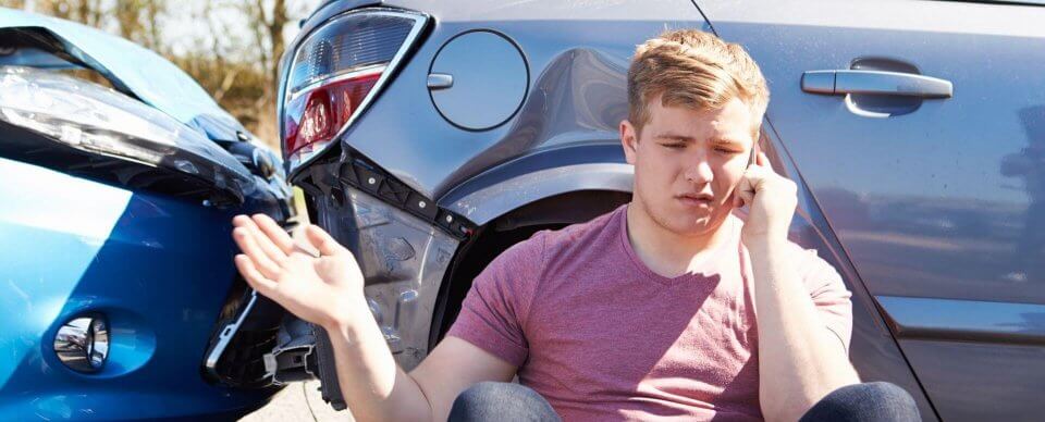 A young man who was just involved in a car crash makes a phone call while looking in despair for how to speed up an auto-insurance claim.