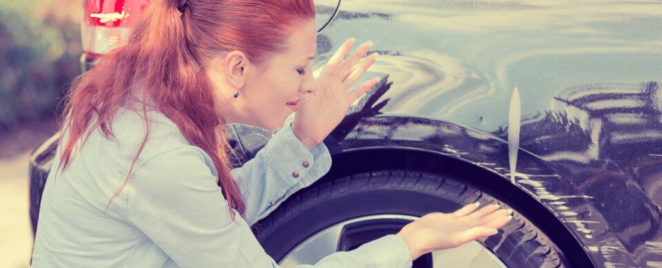 A middle-age Caucasian staring at a dent in her car asking herself Should I file an auto insurance claim.