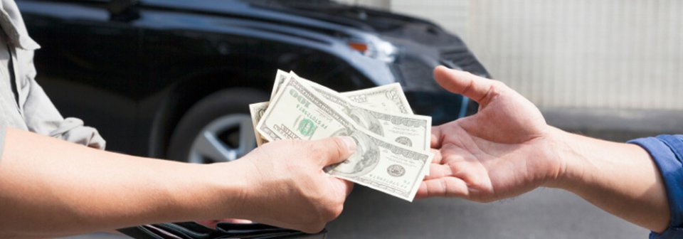 A person handing several dollar bills to another person with an SUV in the back.