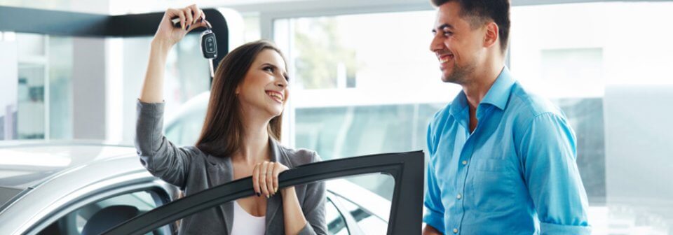 A woman holding car keys while entering a car and smiling at a car dealer that illustrates how new cars might not be as brand-new as you think