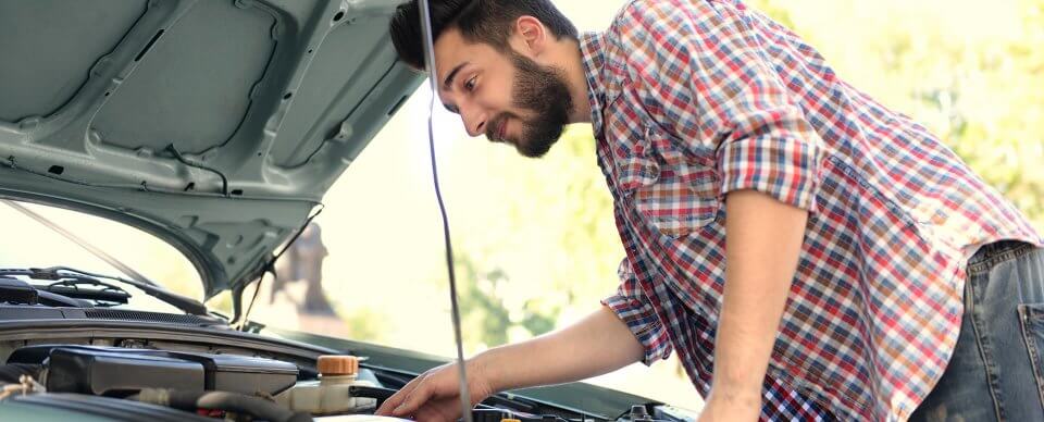 A young, latino man staring at the engine of his car that illustrates how DIY car reparations are not ideal.