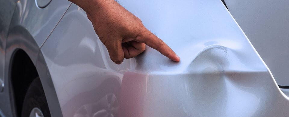 A hand pointing at a dent in a parked car.