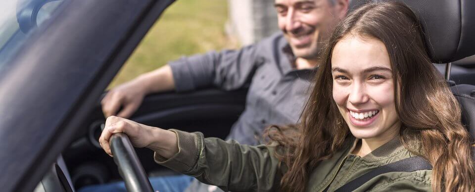 A teenage daughter driving next to her father thanks to teen auto insurance.
