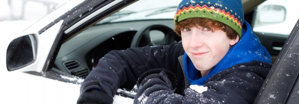 A teenage man driving a car in the snow illustrating 4 tips for teens who will be driving in winter weather.
