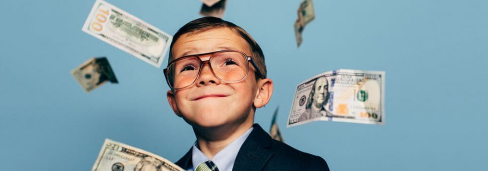 A young child in a suit seeing dollar bills raining around him to illustrate how in auto insurance what you don't know could cost you money.