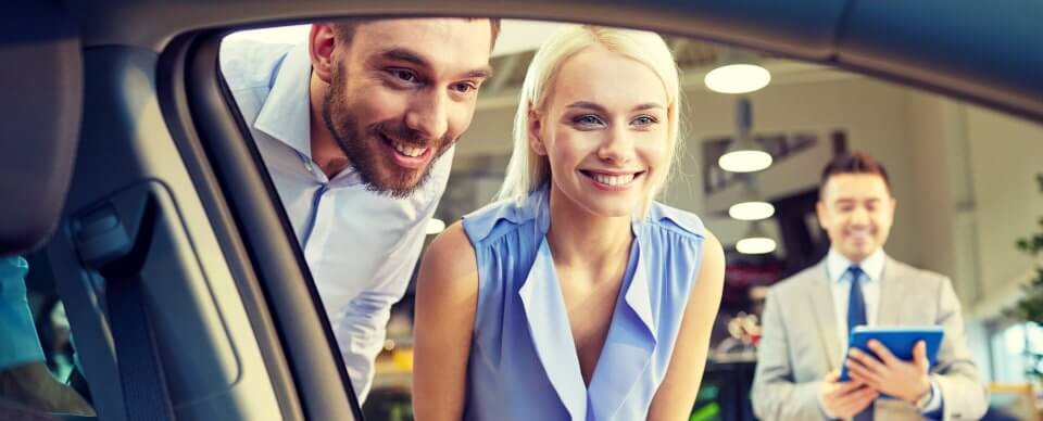 A young, Caucasian couple inspecting a car while car shopping to portray mistakes to avoid.