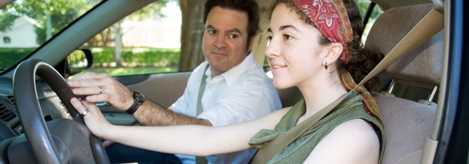 A middle-age Caucasian man teaching his daughter how to drive