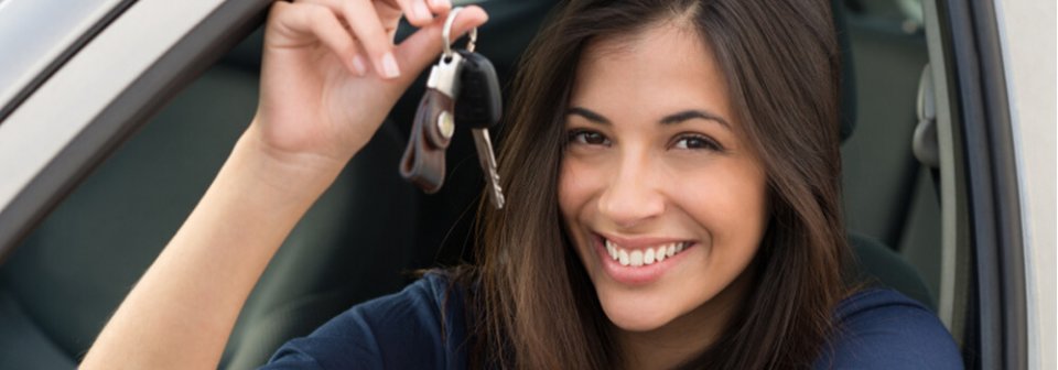 A young brown woman holding car keys and sitting on a car's driver's seat and portraying the 3 worst times to avoid when buying a car.