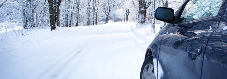 A small sedan driving on a snow-covered road to illustrate what you should know to get around safely while winter driving.