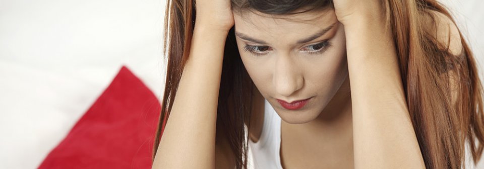 A young Caucasian woman holding her head in confusion because she is confused by all the auto-insurance options and what you need.