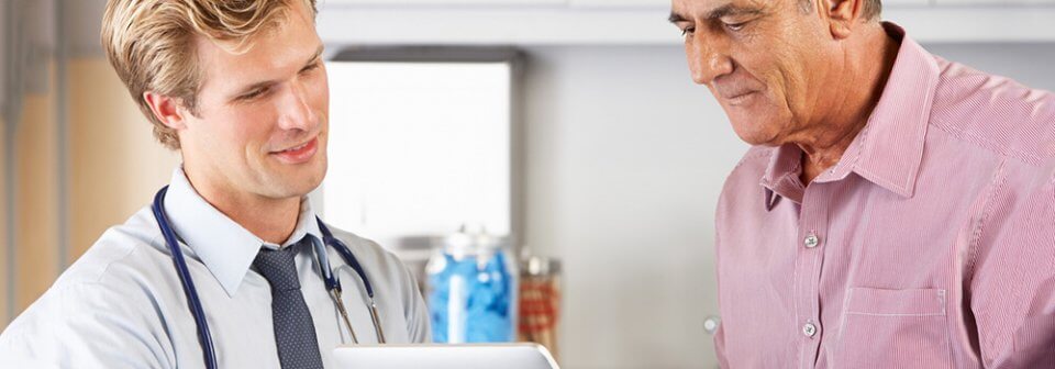 Young, Caucasian man shows healthcare information to an elderly immigrant man and illustrates who qualifies for california healthcare.