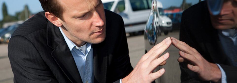 A man inspecting a faulty car to illustrate how not to be taken in when buying a lemon car.