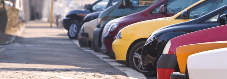 A row of vehicles parked outdoors next to a lonely sidewalk to illustrate whether you should buy more insurance if you park your car outside.