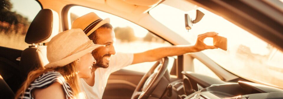 A young Caucasian couple taking a selfie while driving to illustrate how taking selfies while driving could have serious consequences