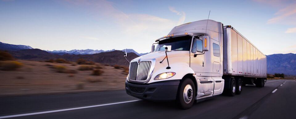 A semi-truck and a trailer driving on a desert road thanks to commercial vehicle insurance.