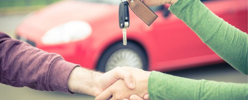 Two people shaking hands after a car sale as the private seller turns the keys to the buyer.