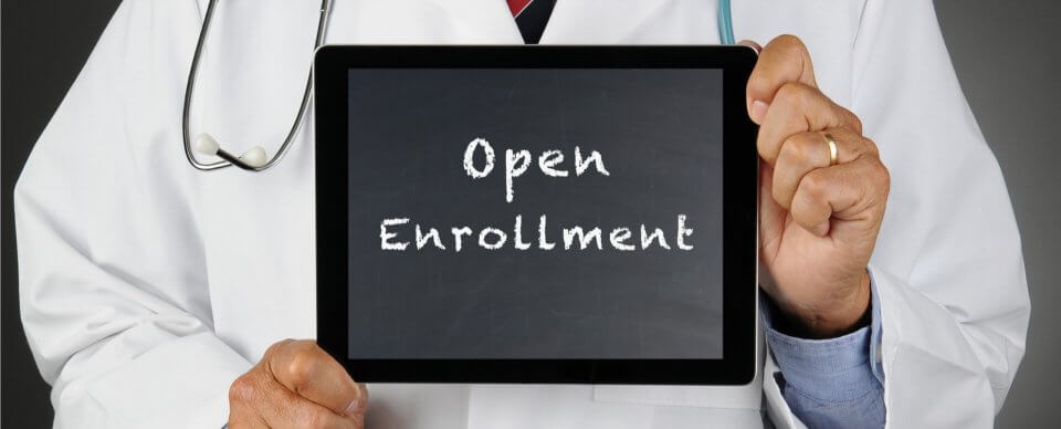 A doctor holding a tablet that reads Open Enrollment to depict what you need to know about open enrollment 2019.