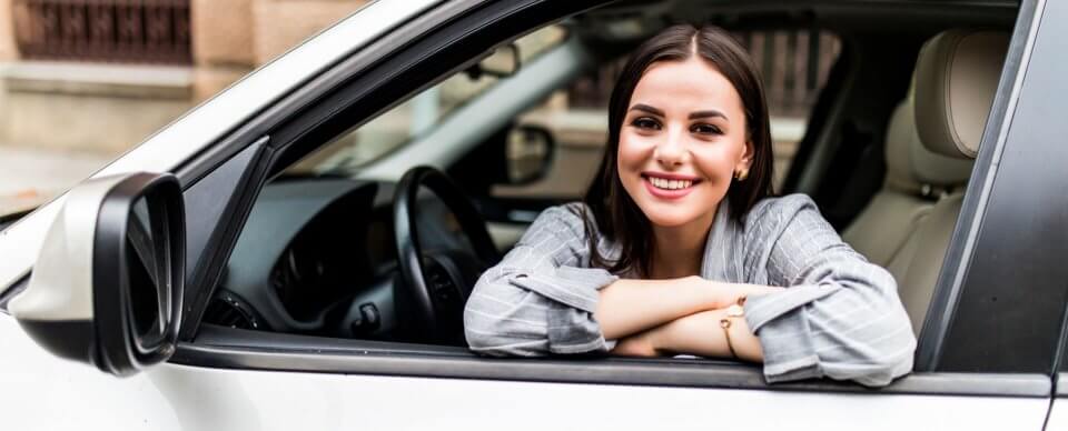 A young, latino woman sitting behind the wheel of a car she just purchased auto insurance for.