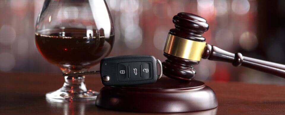 Car keys placed next to a cognac glass and a mallet to portray cases of repeated DUI driving record.