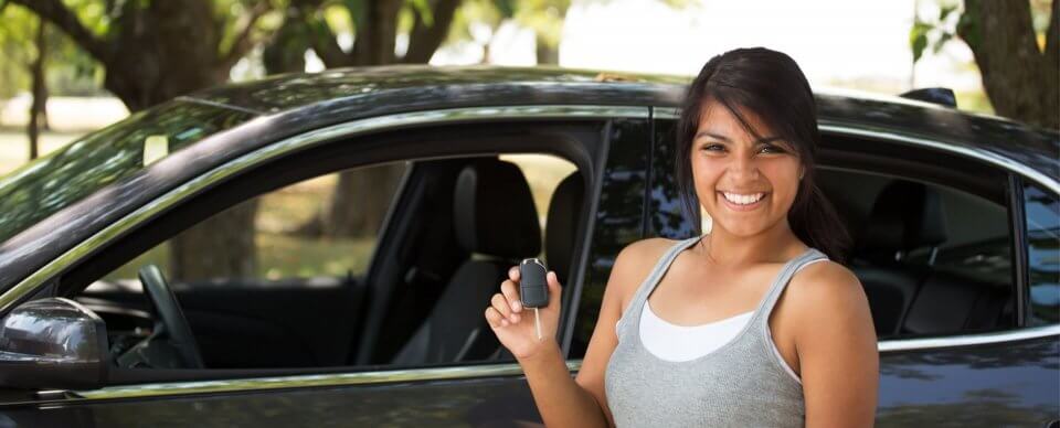 A young latino woman holding the keys to a sedan to illustrate the importance of having car insurance for teens.