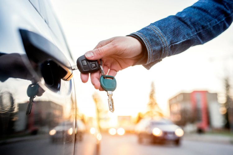 A hand with a car key opening a rental car door to depict why do you need liability with a rental car.