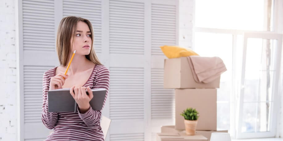 girl sitting in moving boxes with pencil and notebook renters insurance