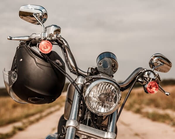 Close-up to a motorcycle handlebar with a helmet hanging from a side to showcase why should i wear a motorcycle helmet