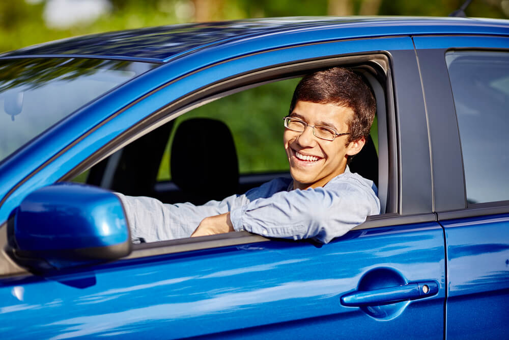 smiling teen driving a blue car young driver insurance