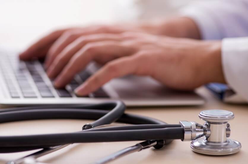 doctors hands typing on computer with a stethoscope telemedicine