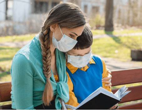 Two children wearing a facemask and reading to illustrate what is social distancing.