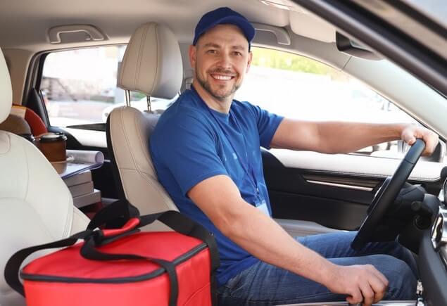 A young, Caucasian food delivery driver in a car with insurance for uber eats