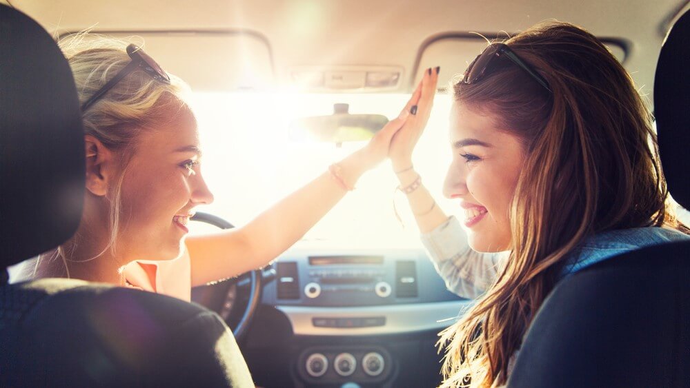 two female friends high five on a car one is a first time driver
