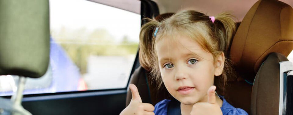 little girl giving thumbs up sitting in a booster seat in a car