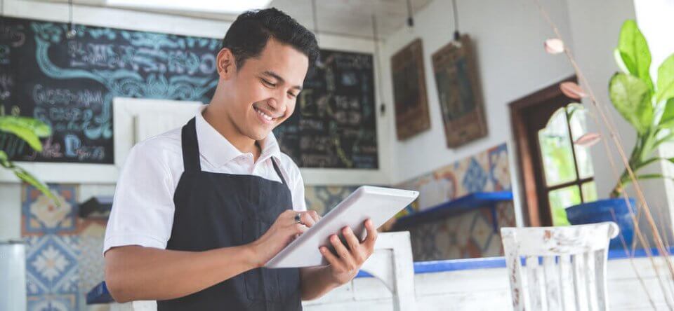 young small business owner at his coffee shop looking at tablet