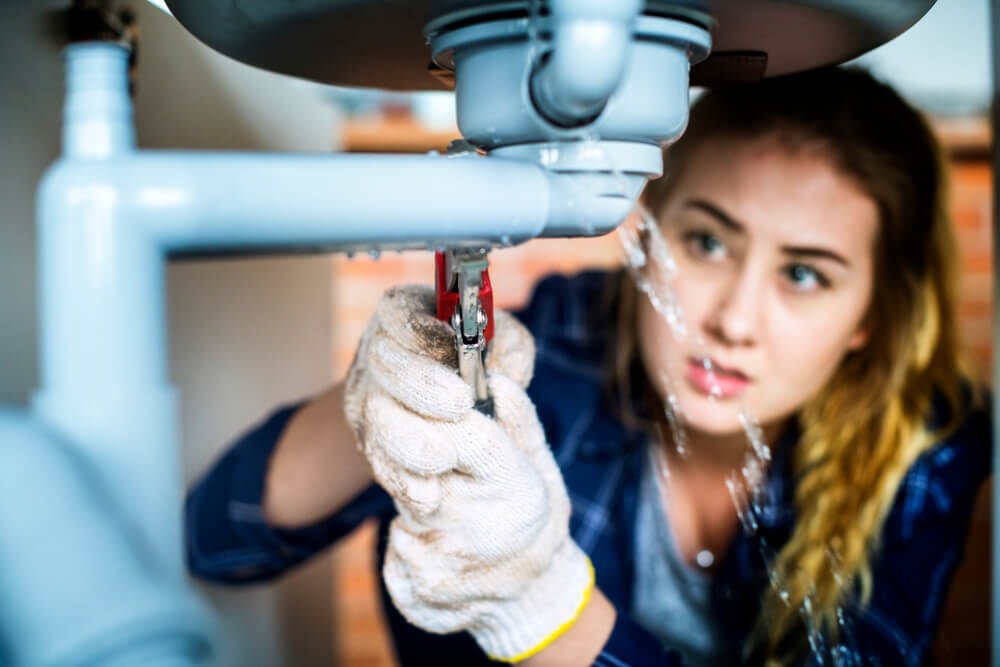 woman trying to fix leak on kitchen sink with homeowners insurance