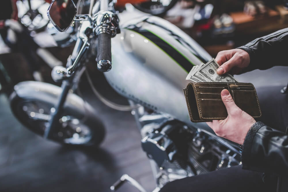 man getting money out of wallet to buy a used motorcycle on the background