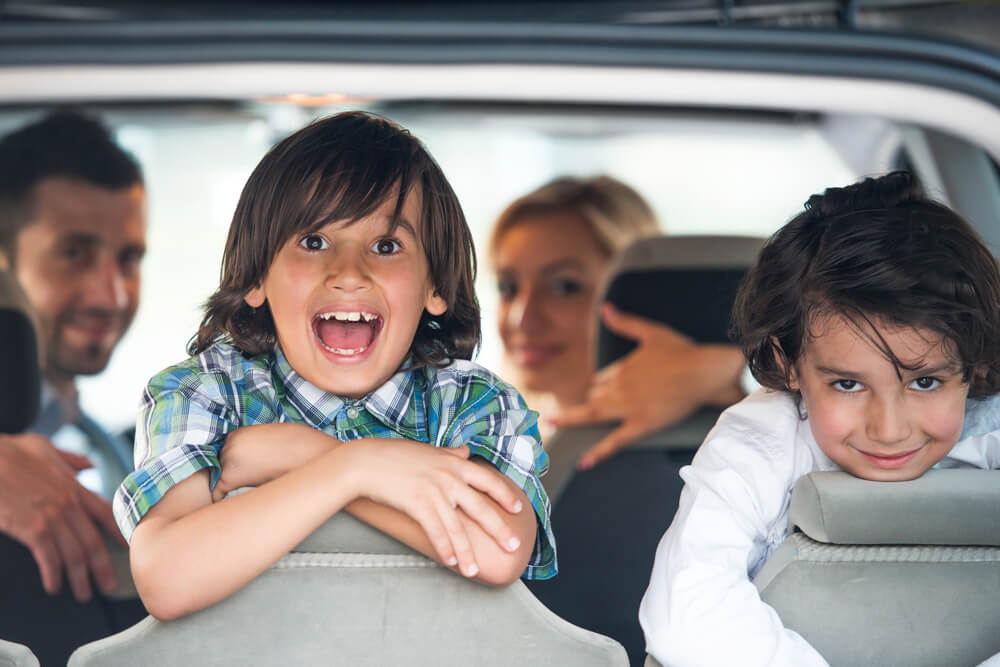 happy children inside car traveling with parents in the background