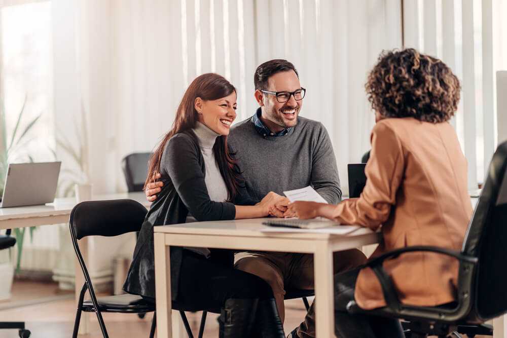 happy couple with insurance broker buying cheap car insurance in office