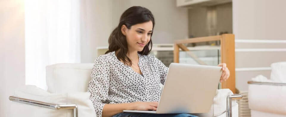 Caucasian woman smiling at her laptop searching for cheap car insurance