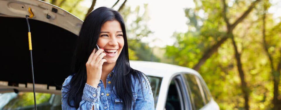 Caucasian woman smiling talking on the phone while waiting roadside assistance for her car.