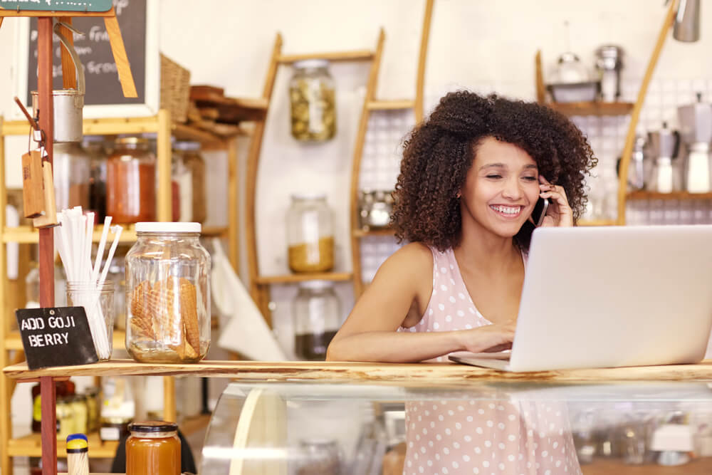 happy young woman in her coffee shop with a laptop and small business insurance