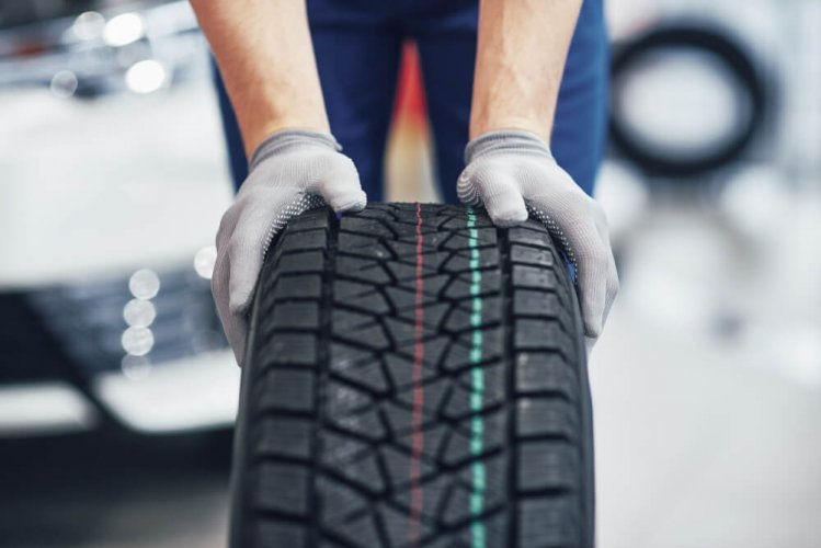 front view of a tire with a technicians hands on it to illustrate how dangerous are worn tires