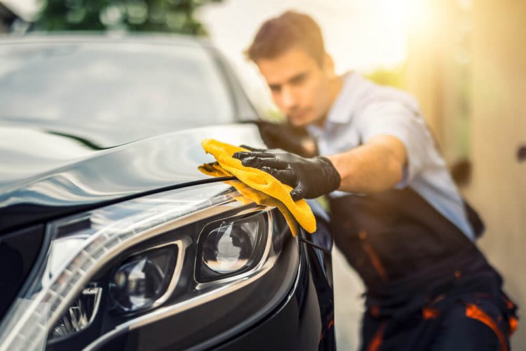 Front view of man detail cleaning car light as part of the annual car maintenance