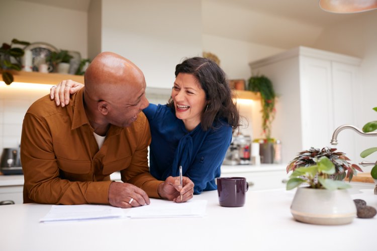 A happy multi-ethnic older couple in their kitchen looking at the types of life insurance