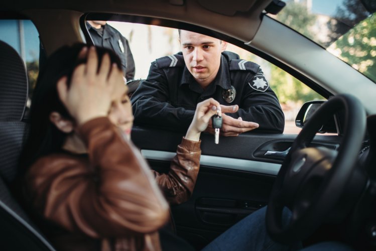 A male traffic officer taking the keys away of a worried woman who commited a DUI.
