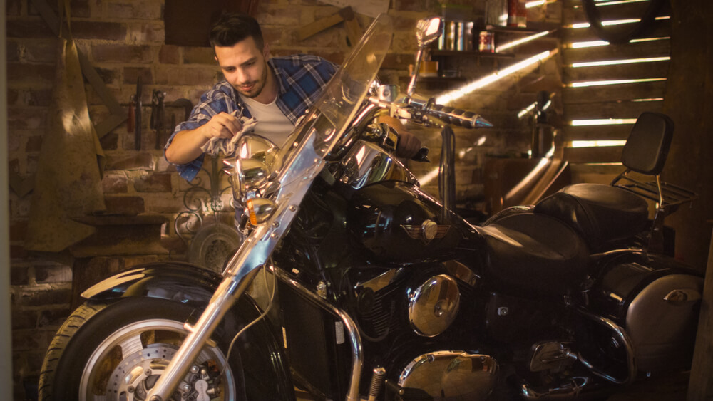 young hispanic man cleaning a motorcycle with cheap insurance in garage