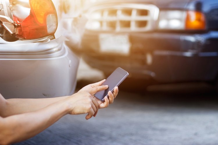 A hand holding a smartphone after being involved in a car accident to illustrate what to do after a car accident.