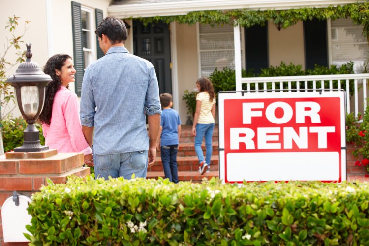 A young multi-ethnic family standing outside a home that is for rent.