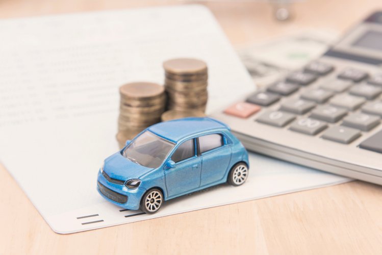 Toy car next to a calculator and coin stacks on wooden table to represent car insurance cost